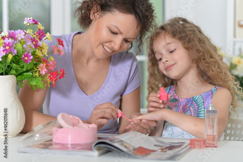 Smiling mother with little daughter  with magazine at home applying nail polish