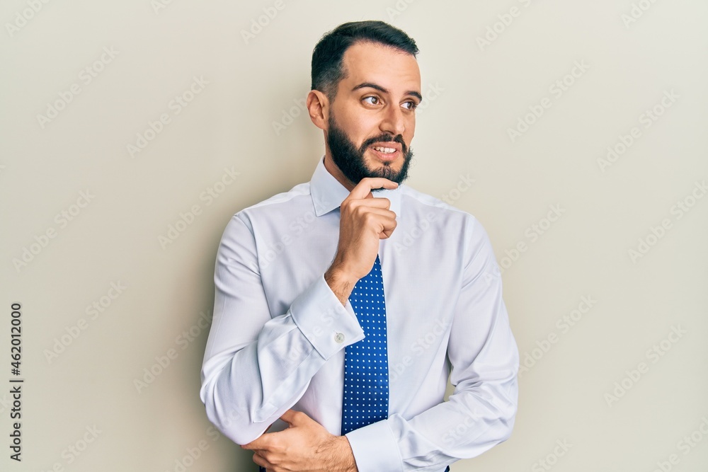 Young man with beard wearing business tie with hand on chin thinking about question, pensive expression. smiling with thoughtful face. doubt concept. Young man with beard wearing business tie with hand on chin thinking about question, pensive expression. smiling with thoughtful face. doubt concept.