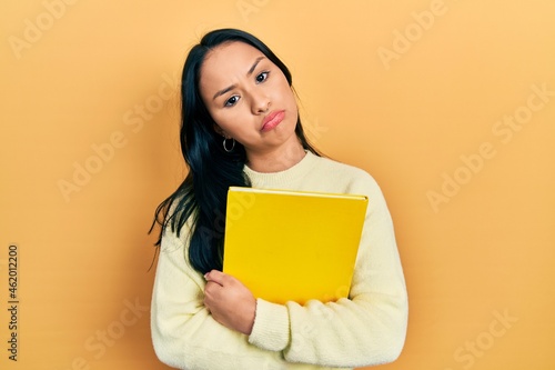 Beautiful hispanic woman with nose piercing holding book depressed and worry for distress, crying angry and afraid. sad expression.