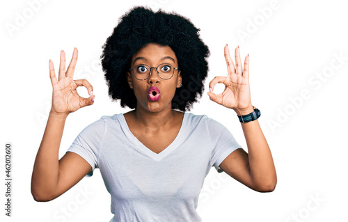 Young african american woman wearing casual white t shirt looking surprised and shocked doing ok approval symbol with fingers. crazy expression