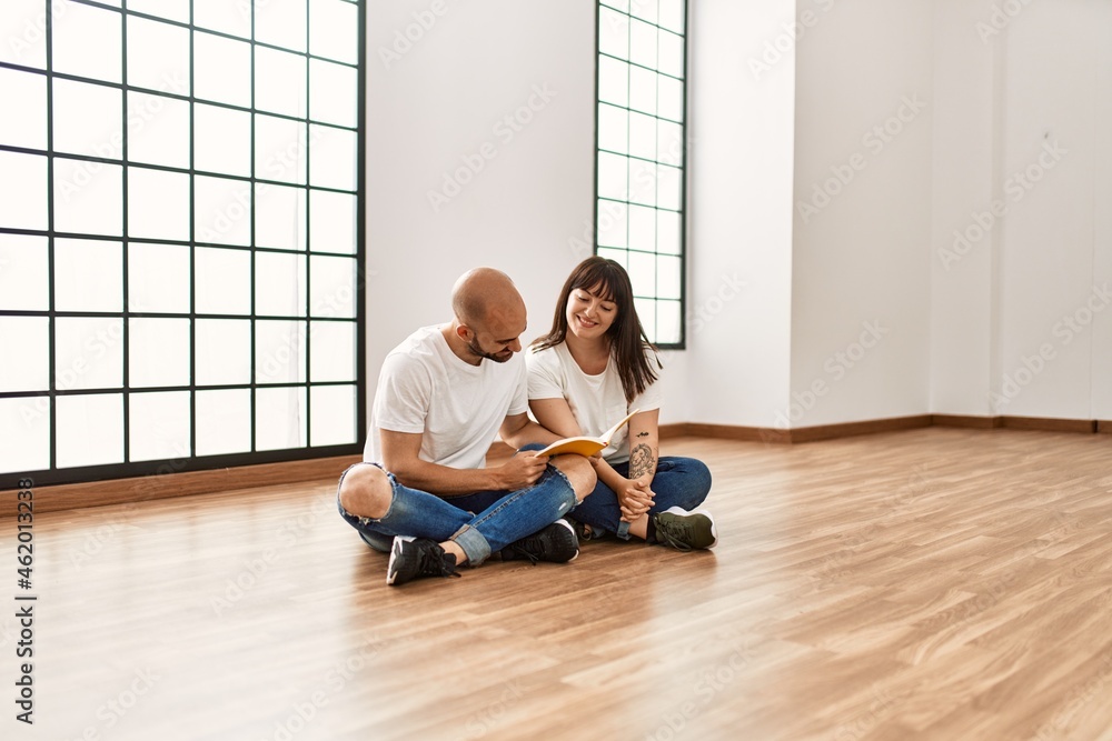 Young hispanic couple smiling happy reading book at empty new home.