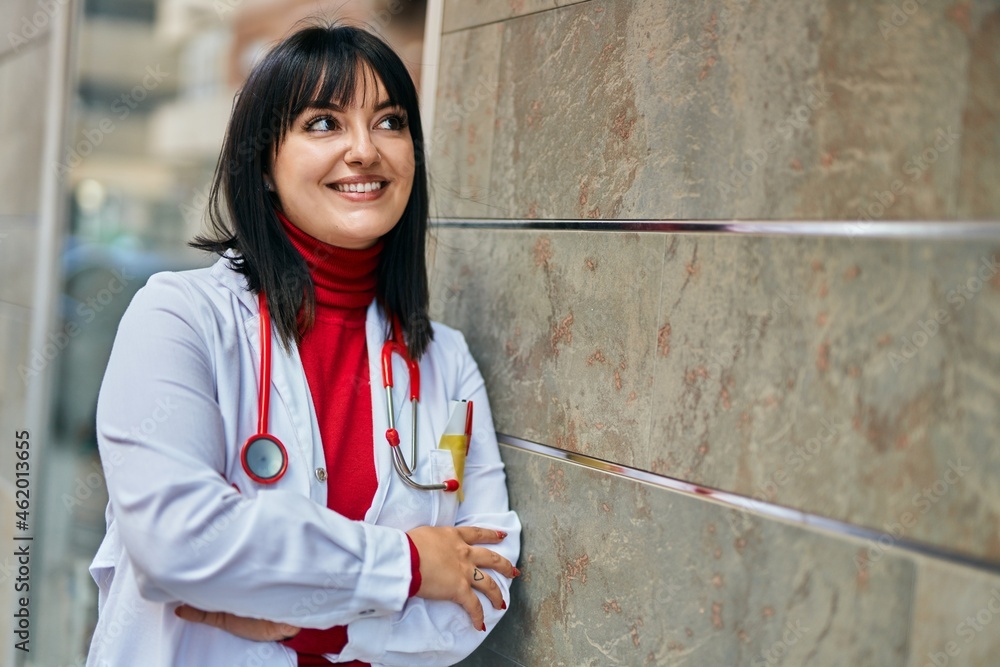 Young brunette woman wearing doctor uniform and stethoscope leaning on the wall