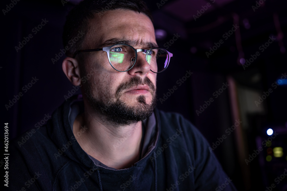 Obraz premium A man stares intently at a computer screen in the dark at night.