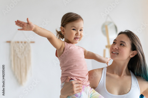 Young mother with little daughter practice yoga home. Warrior pose. photo