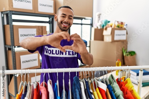 African american man wearing volunteer t shirt at donations stand smiling in love doing heart symbol shape with hands. romantic concept.