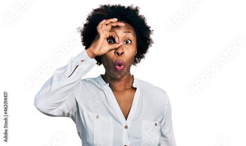 African american woman with afro hair wearing casual white t shirt doing ok gesture shocked with surprised face, eye looking through fingers. unbelieving expression.