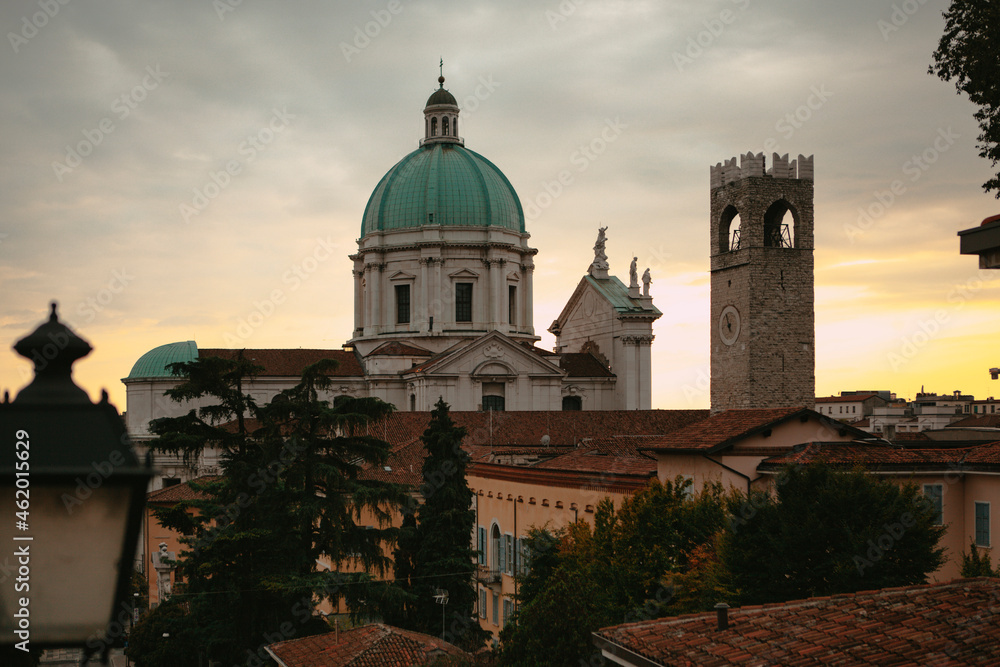 The turquoise dome with stone white sculptures and the tower of the central Catholic church (Duomo Vecchio Cathedral) at sunset in Brescia, Lombardy, Italy. Panoramic view. Italian architecture