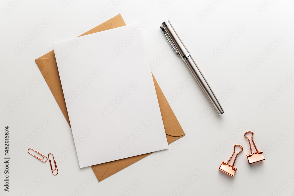 Greeting, wedding or congratulations stationery mockup. Blank sheet of paper on brown envelope, fountain pen and various paper clips on clean desk. Table top view, flat lay, copy space. Greeting, wedding or congratulations stationery mockup. Blank sheet of paper on brown envelope, fountain pen and various paper clips on clean desk. Table top view, flat lay, copy space.