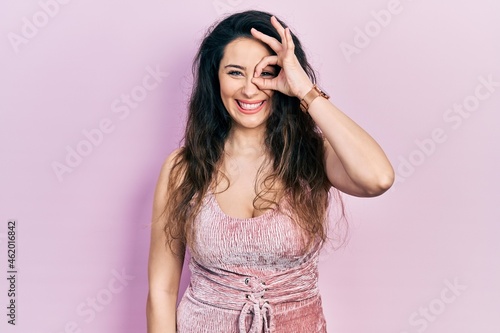 Young hispanic woman wearing casual clothes doing ok gesture with hand smiling, eye looking through fingers with happy face.