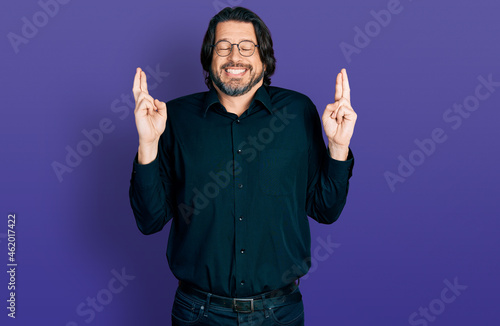 Middle age caucasian man wearing casual clothes and glasses gesturing finger crossed smiling with hope and eyes closed. luck and superstitious concept.