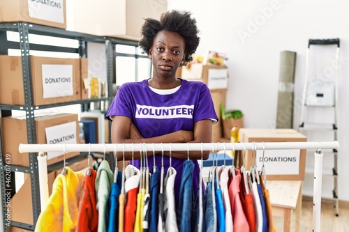 African young woman wearing volunteer t shirt at donations stand skeptic and nervous, disapproving expression on face with crossed arms. negative person.
