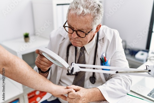 Middle age grey-haired man wearing dermatologist uniform examining skin arm using loupe at dermatology clinic