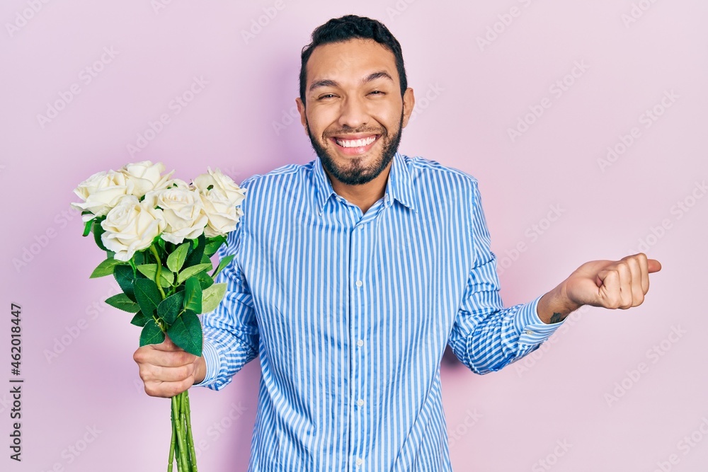 Hispanic man with beard holding bouquet of white flowers screaming proud, celebrating victory and success very excited with raised arm Hispanic man with beard holding bouquet of white flowers screaming proud, celebrating victory and success very excited with raised arm