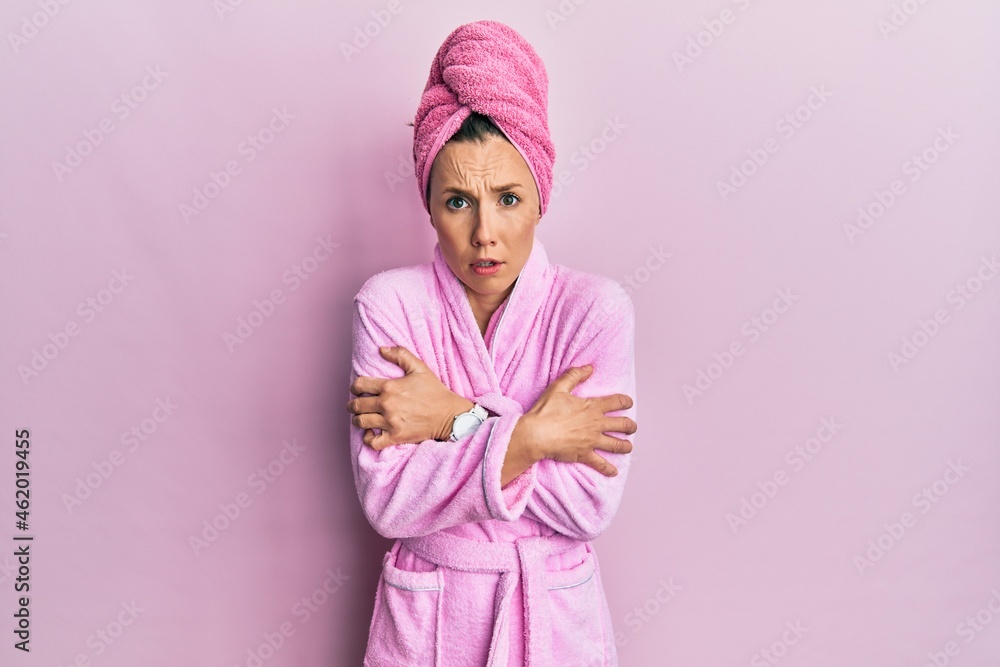 Young blonde woman wearing shower towel cap and bathrobe shaking and freezing for winter cold with sad and shock expression on face Young blonde woman wearing shower towel cap and bathrobe shaking and freezing for winter cold with sad and shock expression on face