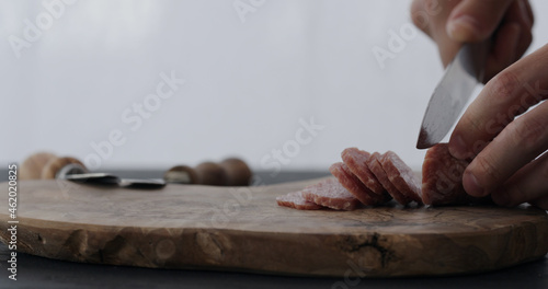 man slicing salami on olive board