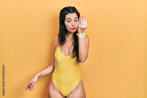 Young hispanic girl wearing swimsuit doing italian gesture with hand and fingers confident expression