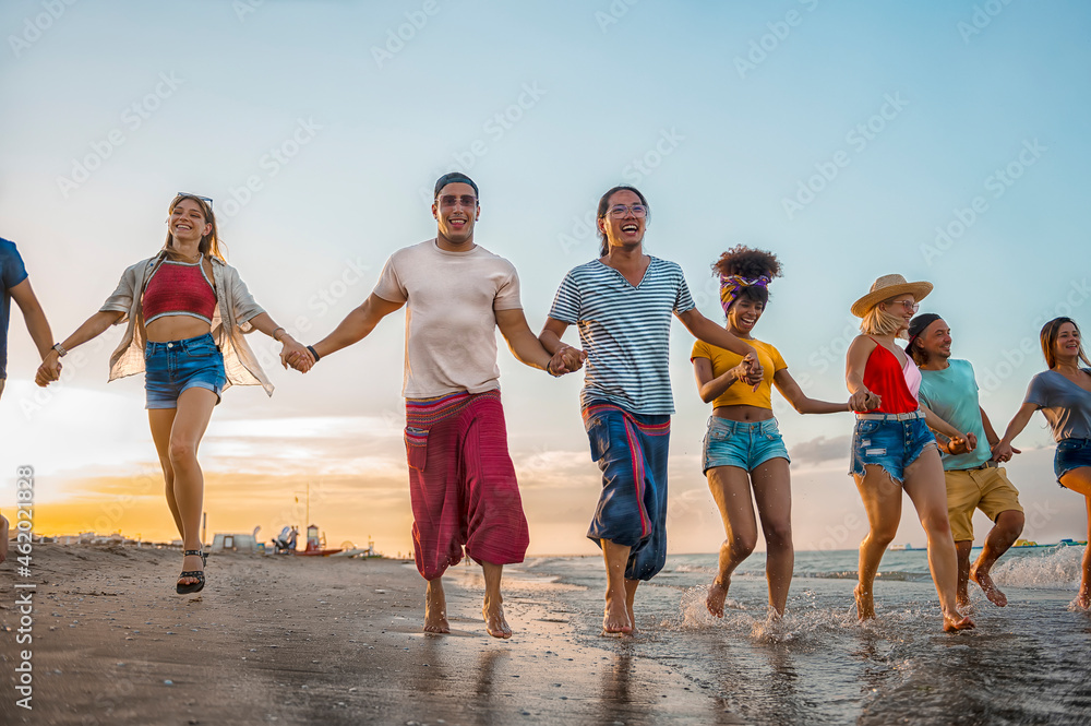 Group of multiracial happy friends at sunset beach party having fun runs to on the beach - Friendship Freedom Beach Summer Holiday Concept