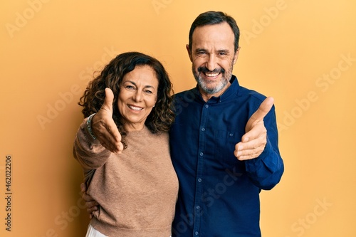 Middle age hispanic couple wearing casual clothes smiling friendly offering handshake as greeting and welcoming. successful business.