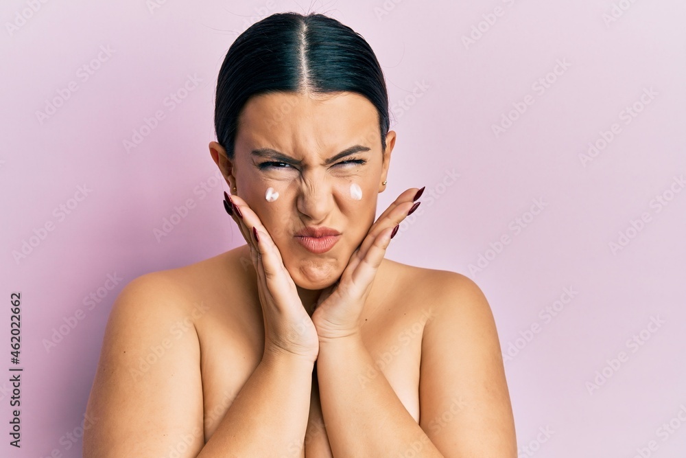 Beautiful brunette woman standing topless wearing face cream skeptic and nervous, frowning upset because of problem. negative person. Beautiful brunette woman standing topless wearing face cream skeptic and nervous, frowning upset because of problem. negative person.