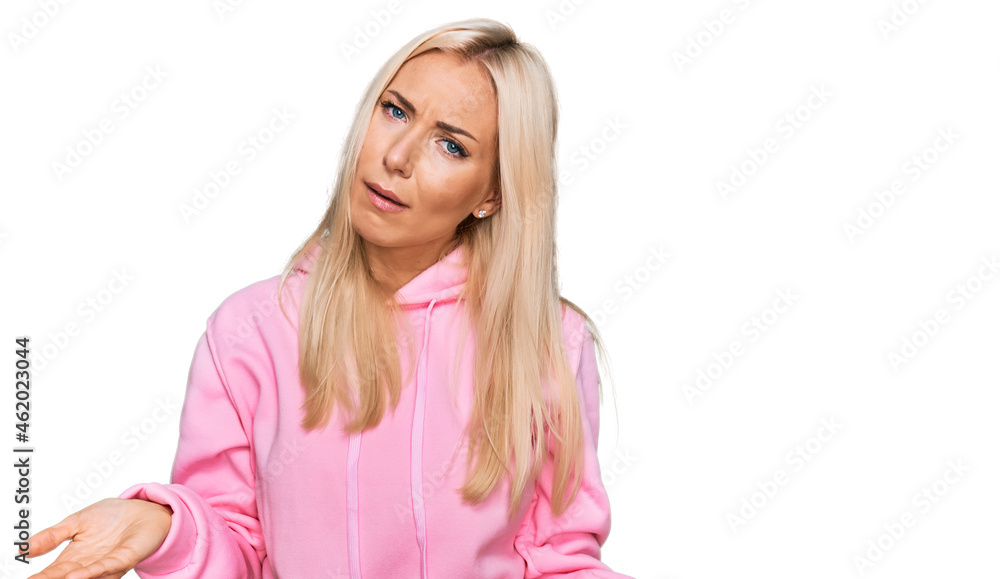 Young blonde woman wearing casual sweatshirt clueless and confused with open arms, no idea concept. Young blonde woman wearing casual sweatshirt clueless and confused with open arms, no idea concept.