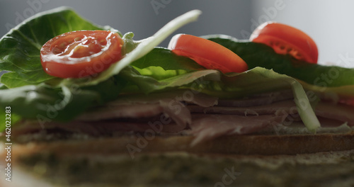 put cherry tomatoes on prosciutto cotto on baguette with cream cheese to make sandwich closeup