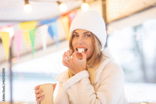 Smiling beautiful girl in knitted hat drinking hot cocoa with marshmallows.