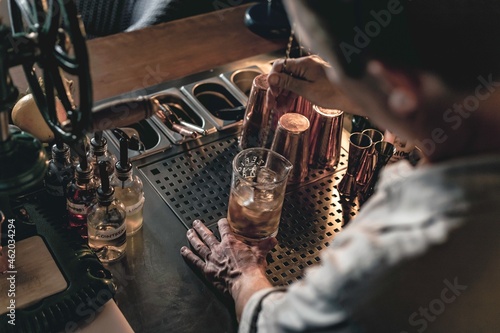 An expert bartender mixing a cocktail in a glass mixer with a long spoon, standing behind the counter of his beautiful cocktail bar in a night club.