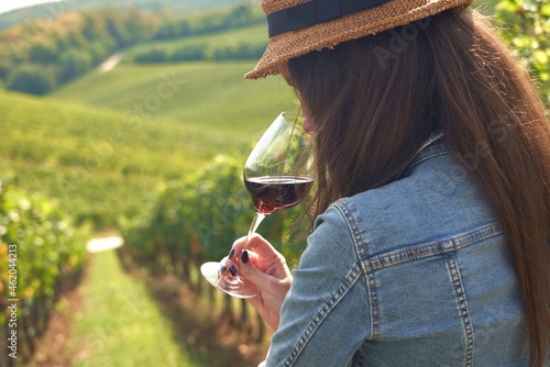 Fotografi Woman holding glass of red wine, tasting in vineyard.