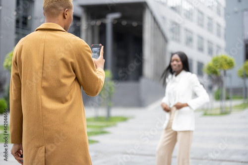 Man taking photo on smartphone of his girlfriend on city street. Concept of relationship. Idea of modern technology. Couple wearing fashion clothes