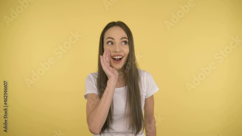 Young attractive woman is 35 years old, sharing a secret with the audience holding hands at the mouth. Young lady on yellow background isolated. 4K