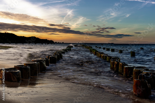 Piękny widok na piaszczyste wybrzeże Bałtyku ze starymi wojskowymi budynkami z czasów II wojny światowej i drewnianymi falochronami. Zachód słońca nad morzem. Zdjęcie o długiej ekspozycji.  © Aneta
