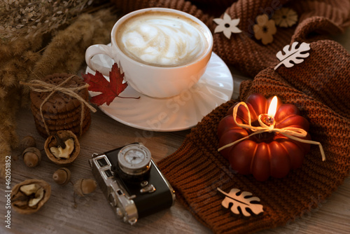 Autumn still life. White ceramic cup with coffee and saucer, cookies, walnut, burning candle like a pumpkin, acorns and warm knitted sweater