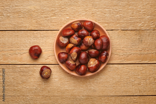 Horse chestnuts in bowl on wooden table. Autumn nature harvest. Top view with copy space.