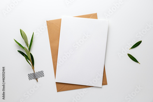 Blank greeting, invitation, congratulation or condolence card beside an olive branch (symbol for life, peace, love and loyalty), fixed on a white desk with washi tape. Top view, flat lay, copy space.
