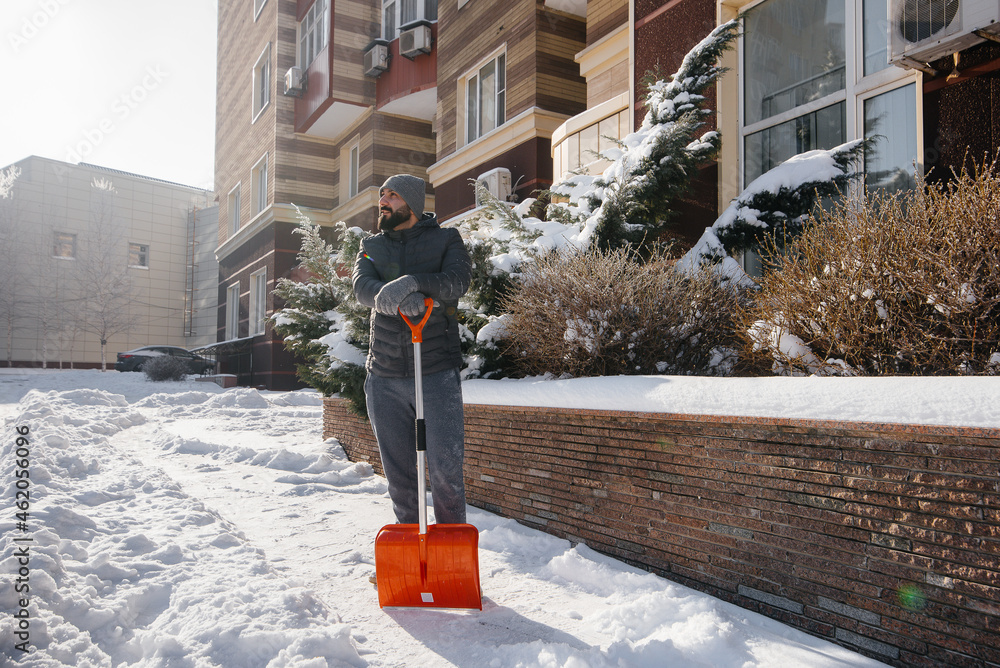 A young man clears the snow in front of the house on a sunny and frosty day. A young man clears the snow in front of the house on a sunny and frosty day.