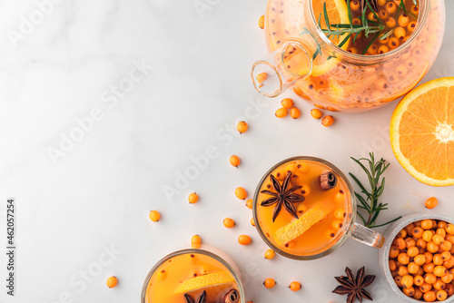 Sea buckthorn autumn tea with orange in glass cups with fresh berries, cinnamon and rosemary on white table. Top view