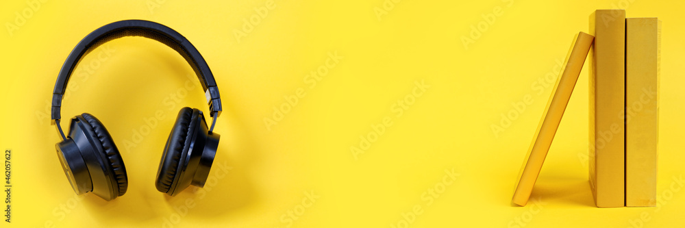 Headphones and books on vibrant color yellow background. Listen to books audiobook concept. Headphones and books on vibrant color yellow background. Listen to books audiobook concept.
