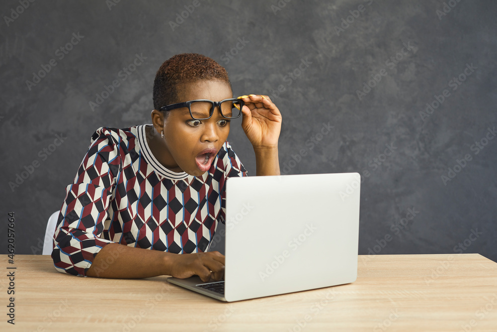 WOW. Surprised shocked African American woman sitting at desk and looking open-mouthed at screen of laptop computer. Young black lady wins prize, gets job offer, receives email with unbelievable news - obrazy, fototapety, plakaty 