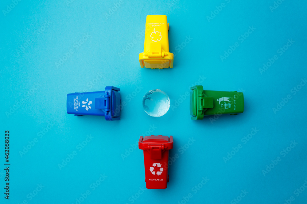 The concept of Earth Day is a global problem of consumer society. Garbage cans of different colors with the recycle logo around the planet Earth on a turquoise background. Copy space. Top view The concept of Earth Day is a global problem of consumer society. Garbage cans of different colors with the recycle logo around the planet Earth on a turquoise background. Copy space. Top view