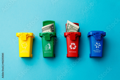 The concept of the collapse of the dollar. Wasted money is the same as being thrown in the trash. Trash cans of different colors with the recycle logo with discarded money on a turquoise background