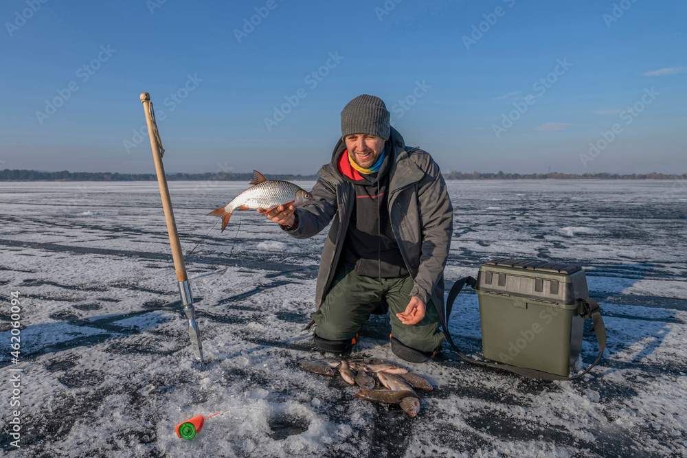 Winter ice fishing. Fisherman on lake catch roach fish from snowy ice