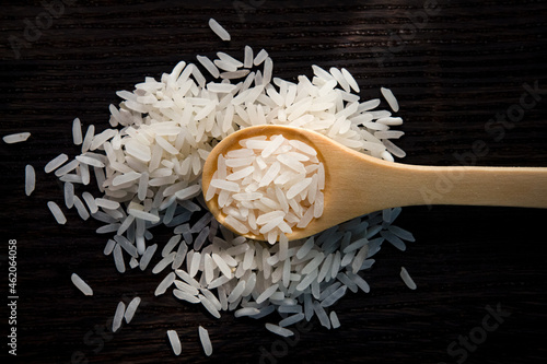 Top view of white rice in wooden spoon on dark wooden table. 