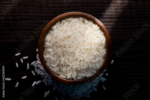 Top view of white rice in wooden bowl on  dark wooden table.