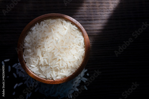 Top view of white rice in wooden bowl on dark wooden table