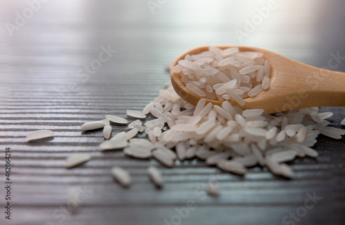 White rice in wooden spoon on dark wooden table. Selective focus.