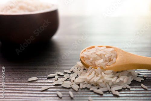White rice in wooden spoon on dark wooden table. Selective focus.