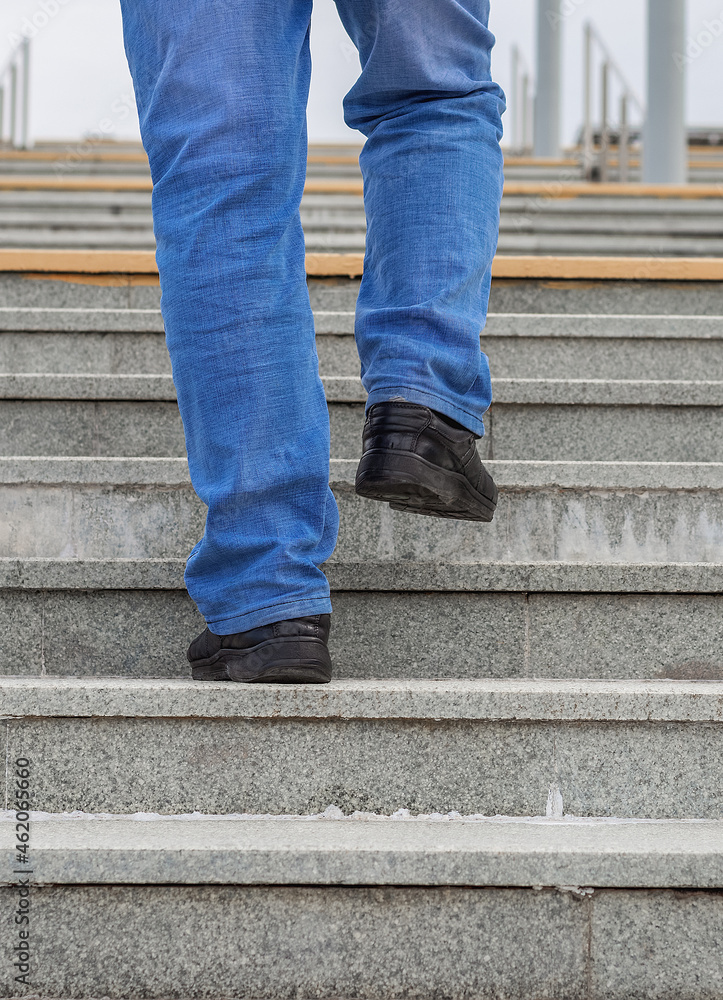 Male legs in jeans and boots climb the stairs.