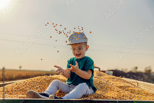 Fotografía A smiling little boy sits on the corn grains in a tractor-trailer and playing with them during corn harvest