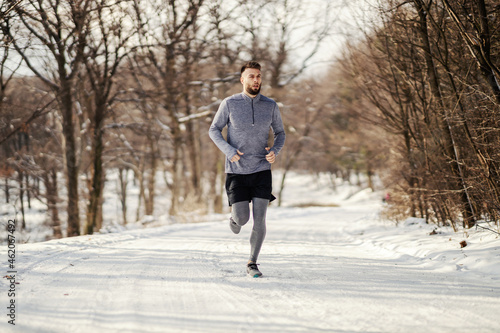 Sportsman running on snowy path in nature, Winter fitness, outdoor fitness, healthy life.