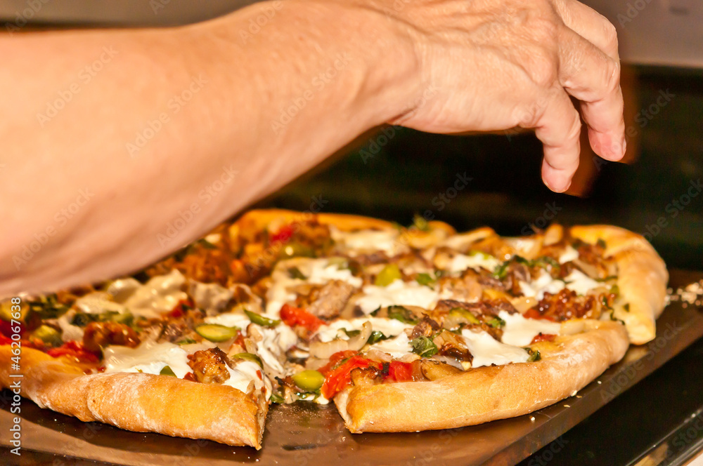 top, front view, medium distance of a chefs hand separating the cut slices of baked pizza to plate the slice for his guests